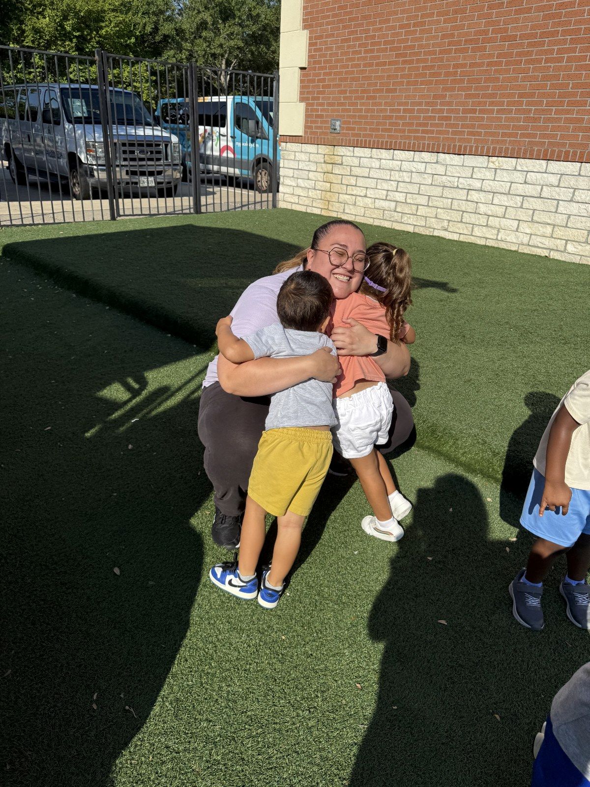 A MyPlace teacher hugging two happy children on the playground