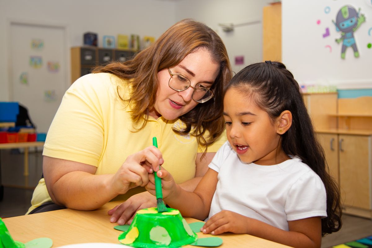 A teacher guiding a preschooler through a hands-on craft at MyPlace, Katy TX